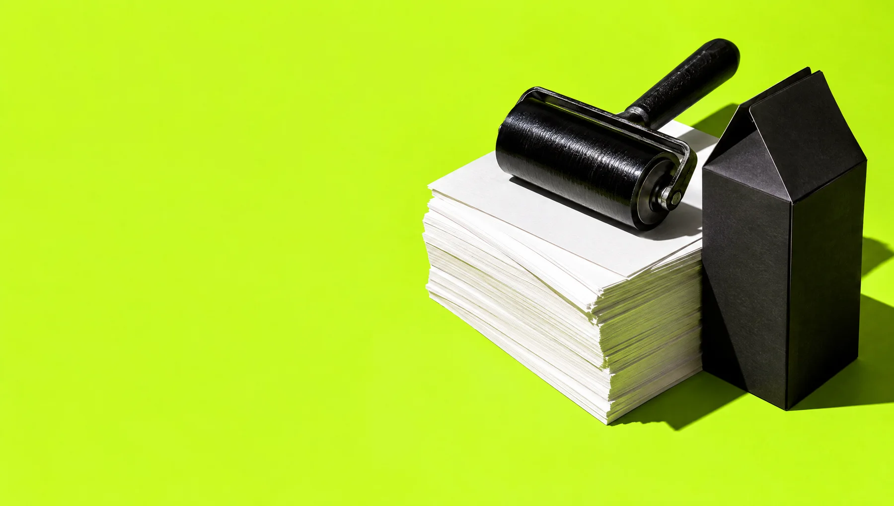 An ink roller and folded black carton on stacked lime and white paper